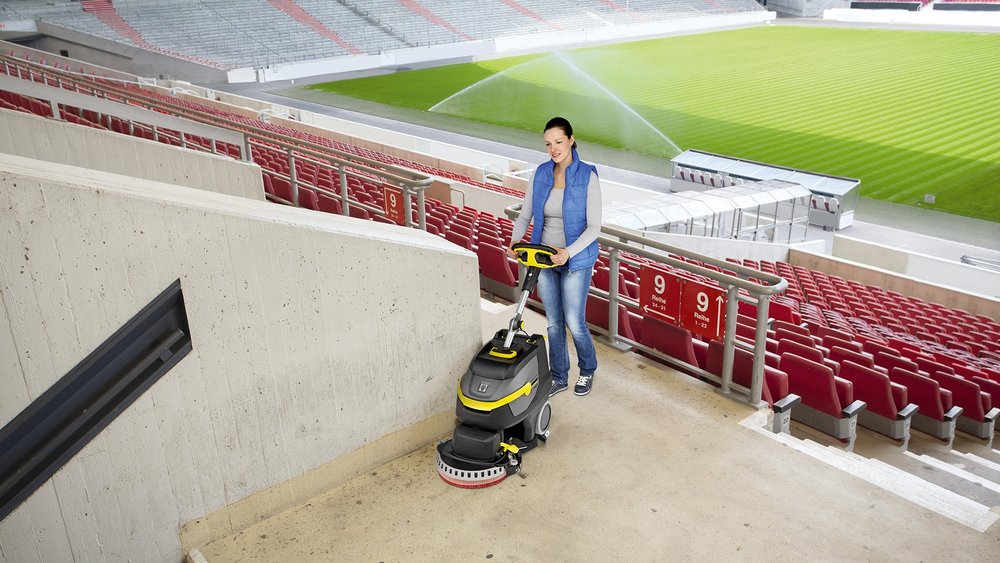 Handgeführte Scheuersaugmaschine beim Reinigen einer Fläche in einem Fußballstadion